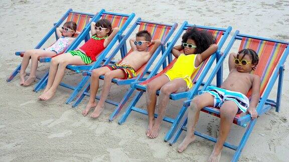 暑假一群不同的孩子在热带海滩一起躺在沙滩椅上休息