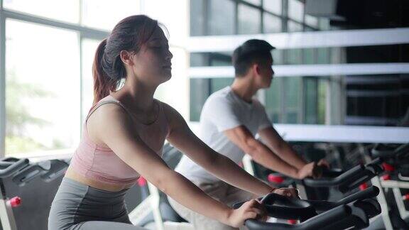 亚洲女人和男人在健身房进行自行车训练