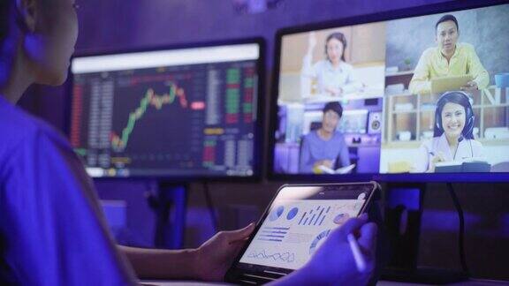 年轻的女企业家拿着数字平板电脑使用多个电脑屏幕学习投资金融同时与她的伙伴进行视频电话会议