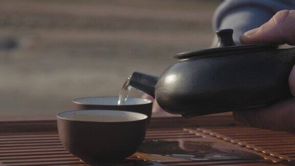 一个男性的手从一个粘土茶壶倒茶从宜兴到碗的特写手工制作的泥茶壶中国茶道4k的视频23.98帧秒