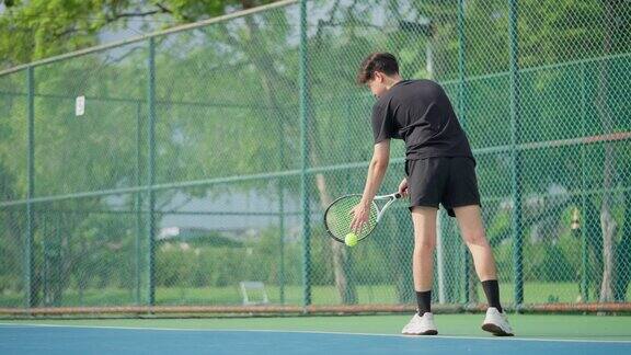 一名男子网球运动员正在室外场地上弹起准备发球的网球然后在击球后发球