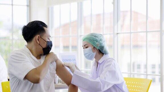 COVID-19疫苗接种站医生或护士正在病房为男性患者接种COVID-19或流感疫苗人们在诊所或医院办公室佩戴口罩以预防病毒感染
