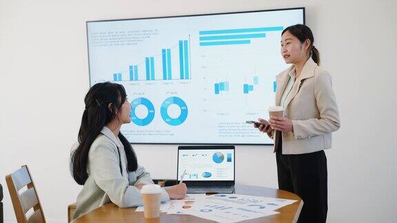 年轻的成年女性理财顾问一边在会议室向客户授课和演示一边在大电脑屏幕上用图表向客户解释投资