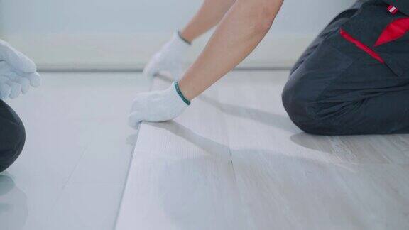 工匠或木匠们戴着手套双手合十在走廊上铺设拼花地板工作木工施工团队在地板上安装强化板以修复和翻新公寓或房子
