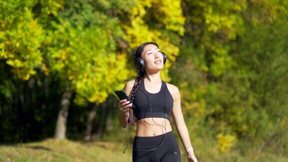 年轻开朗活跃的运动女孩走耳机手机享受听音乐慢跑在城市公园或森林背景的亚洲女人