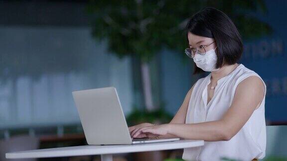 亚洲商界女性在干净现代、没有新冠肺炎的办公室里戴口罩保持社交距离利用高速互联网技术在线工作视频会议