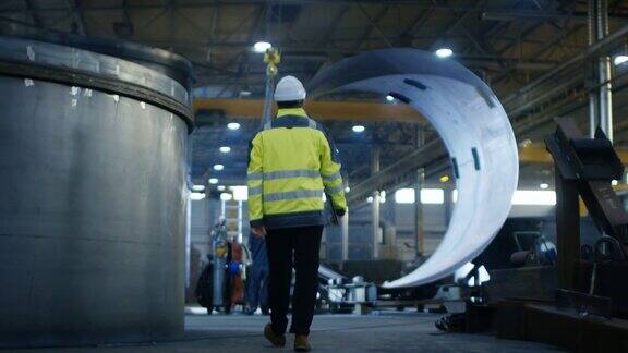 工业工程师戴安全帽穿安全夹克走过重工业制造工厂与各种金属加工过程的后视图