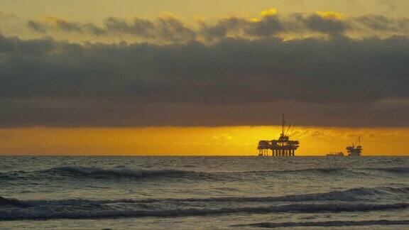 海浪撞击海岸亨廷顿海滩在南加州与几个剪影的近海石油钻井平台和石油(石油)油轮在地平线上的距离在日落下一个戏剧性的暴风雨的S