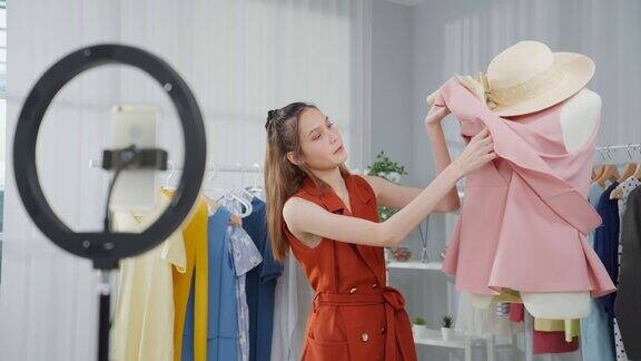 亚洲美女对着镜头说话在家里卖衣服年轻有吸引力的商人通过虚拟在线直播工作在商店向顾客展示和销售服装产品