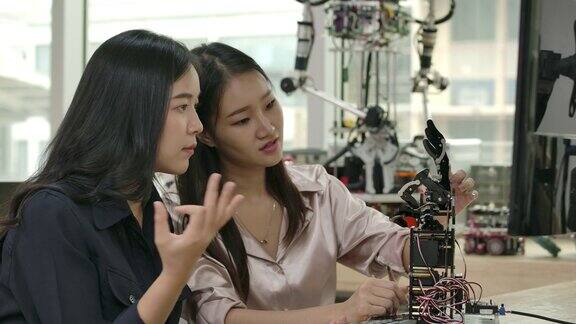 女电子工程师在实验室里建造、测试、修理机器人两位亚洲女性为机械机械手创造运动有技术或创新观念的人