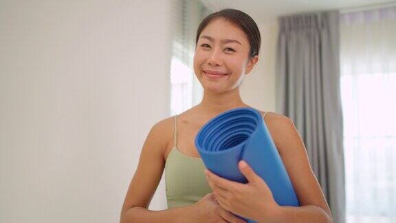 近距离拍摄快乐漂亮的女人穿着运动女性胸罩拿着瑜伽垫站在客厅里微笑健康和积极的生活方式瑜伽练习后精神焕发运动