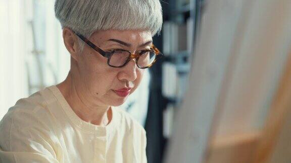 特写手亚洲老年妇女年长的人成熟的女士戴眼镜坐在椅子上使用画笔在画布上创造抽象艺术品在家里的车间