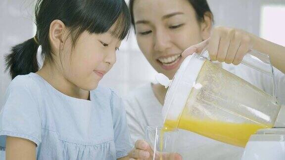 孕妇和她的女儿从搅拌机倒水果冰沙在玻璃杯里