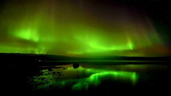 北极光滚过一个湖-一层明亮的滚动北极光反射在一个岩石湖的时间推移视频