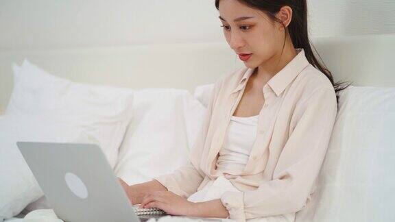 亚洲女商人使用技术笔记本电脑工作在线学习和写笔记本在床上