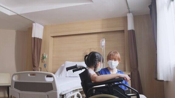 亚洲擦洗女护士照顾女孩小孩病人坐在轮椅上在医院恢复室身着制服的女医务人员推着轮椅来到窗前微笑着和小女孩交谈