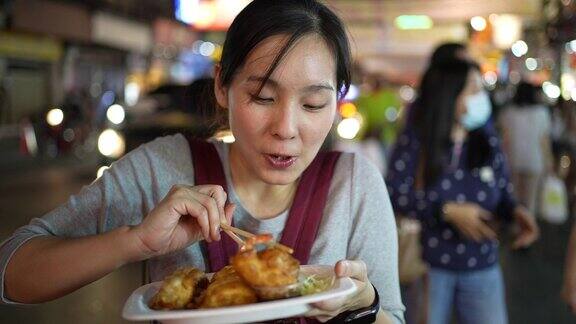 年轻的亚洲女人在街上吃街头小吃