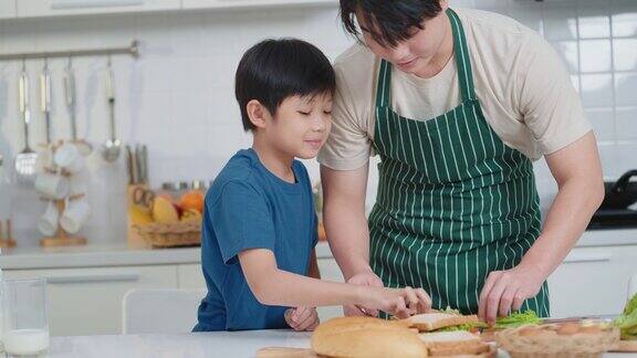 快乐的亚洲爸爸和可爱的小男孩在厨房做三明治当早餐家庭时间健康零食