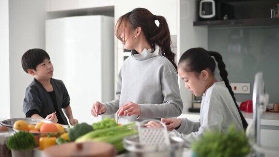 亚洲中国母亲和女儿儿子在厨房里切碎胡萝卜准备凉拌卷心菜沙拉