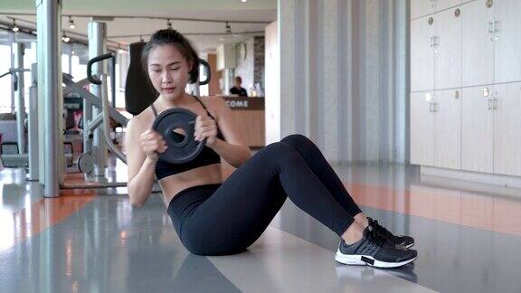 专业美丽的亚洲妇女锻炼做坐起与重量板运动在健身馆健康的生活方式运动员腹肌建立强壮和健康的身体4k分辨率