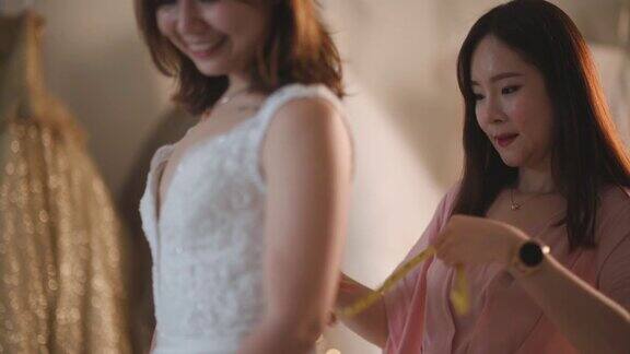 亚洲华人女婚纱店老板正在为顾客测量新娘的体型为顾客量身定制婚纱