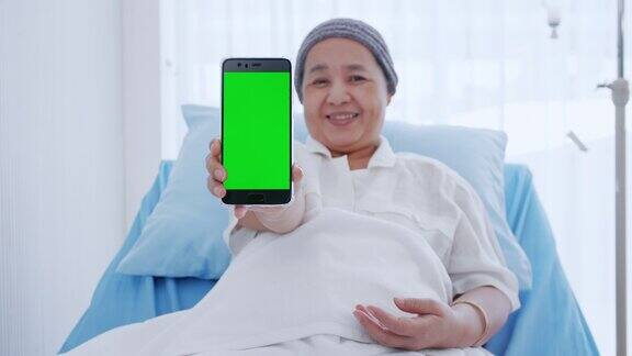 一位身患癌症的老年妇女坐在床上正在用她的智能手机显示一些信息