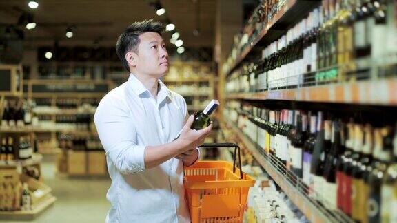 亚洲男性在酒类商店或超市选择葡萄酒男买主检查了这瓶酒然后把它放在一个篮子里