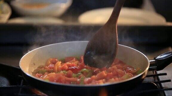 用平底锅煎西红柿和辣椒准备饭菜用搅拌勺搅拌食物