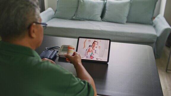 男性在家里的客厅与女医生在数字平板电脑上进行远程视频通话