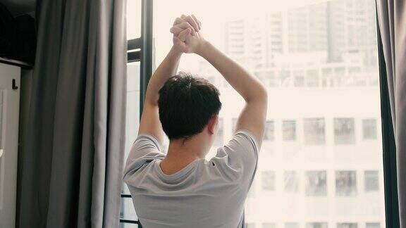 一个男人醒来拉开窗帘伸伸腰生活方式简单的生活