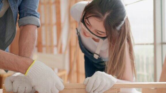 快乐的亚洲年轻成年女性练习使用工作工具成为一个木匠在一个木制DIY车间锤子在一个钉子的帮助并从专业木匠成人学习爱好