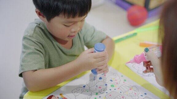 快乐的亚洲男孩与他的母亲在家里的客厅画水彩画