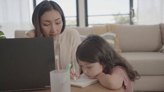 亚洲母亲帮助学龄前的女儿女孩在家里使用笔记本电脑电子学习放大在线虚拟课堂家庭教育新常态