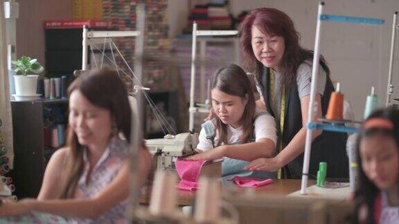 亚洲华人成熟女性裁缝在她的工作室里教她的缝纫班学生缝纫技巧