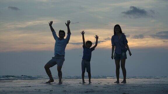 在夕阳的背景下欢乐的一家人在海滩上跳跃的剪影慢镜头家庭、自由和旅行