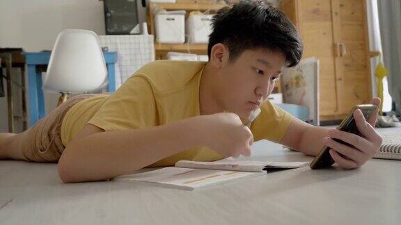 亚洲男孩躺在地板上做作业同时在家学习在线课程社交距离的生活方式概念