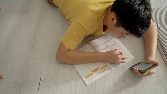亚洲男孩躺在地板上做作业同时在家学习在线课程社交距离的生活方式概念