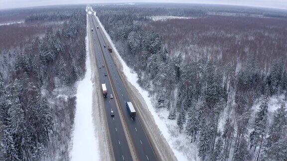 几辆卡车在高速公路上行驶经过一片白雪覆盖的森林