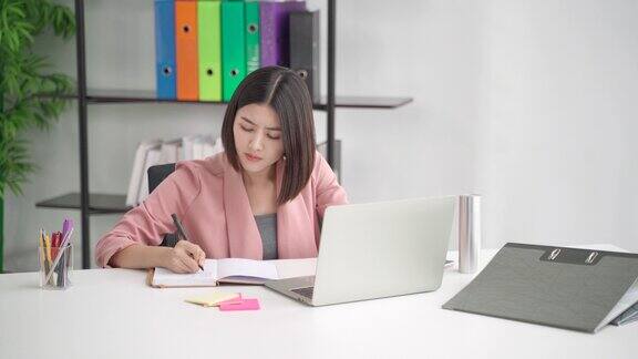 专注专注的亚洲女商人专业工作者写笔记规划思维创意创意策略员工努力工作在现代办公室使用笔记本电脑技术