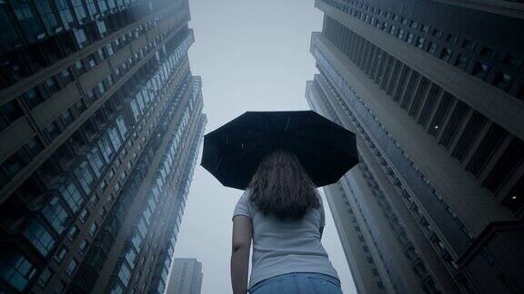 打着伞的女人站在雨中仰望摩天大楼