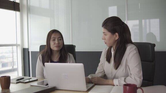 2名亚裔华裔白领在开放式办公室看着笔记本电脑讨论