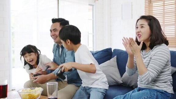快乐亚洲家庭爸爸妈妈和孩子有趣的玩电子游戏与技术控制台在家里的客厅