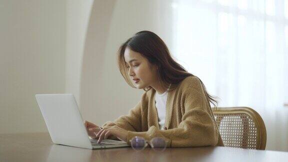 微笑的亚洲年轻女性在家里的笔记本电脑上工作年轻的亚洲学生使用计算机远程学习虚拟培训电子学习观看在线教育在家里的网络研讨会