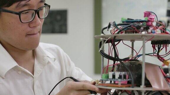 年轻的亚洲电子开发工程师与机器人一起工作在车间测量机器人原型电路中的信号有技术或创新观念的人