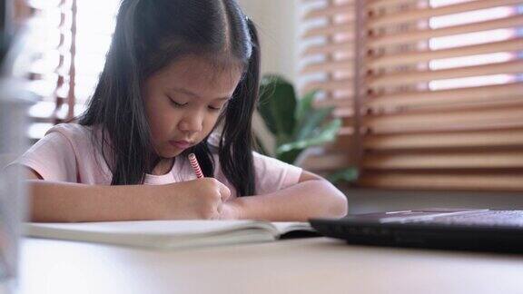 专注的小女孩在家用笔记本电脑上网学习并做笔记