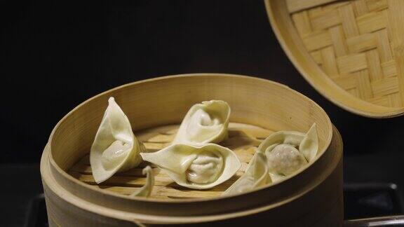 一个男人的手打开了竹制蒸笼盒的盖子上面显示着中国饺子馄饨在黑色的背景上中国菜餐厅亚洲蒸菜点心饺子慢动作