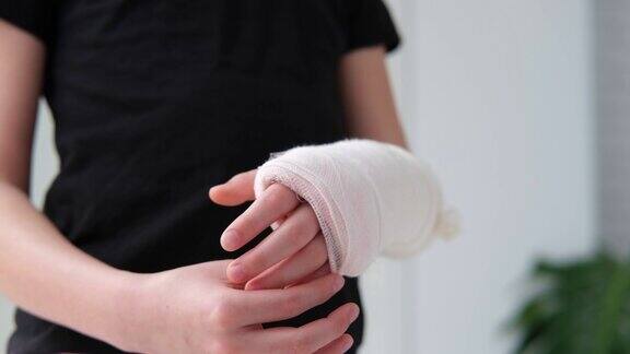 孩子在用白色石膏绷带包扎的断手手指上做按摩医疗保健女孩拿着一条断了的胳膊背景是一件黑色的t恤