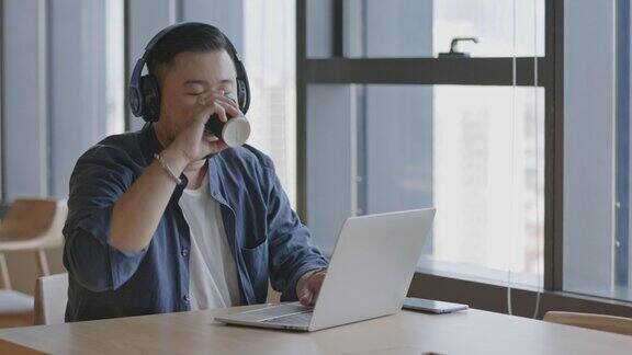 年轻的亚洲商人戴着耳机坐在办公室里在笔记本电脑上进行在线会议概念数字体验