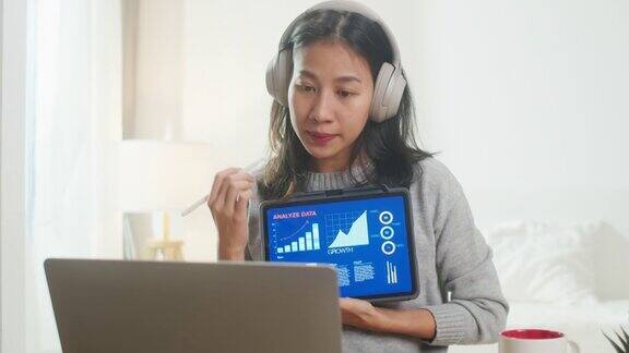 亚洲女商人戴着耳机用笔记本电脑与同事视频通话同时在卧室智能工作