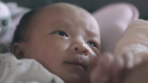 一个刚醒来的亚洲新生儿的脸部特写在妈妈的怀里有一个愉快的可爱的心情